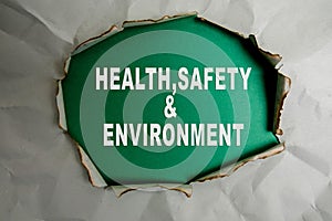 HEALTH, SAFETY AND ENVIRONMENT CONCEPT text at plain torn paper.