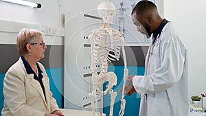 Health specialist examining human skeleton with senior patient