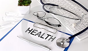 HEALTH text on white paper on white background. stethoscope ,glasses and keyboard