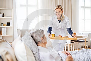 A health visitor bringing breakfast to a sick senior woman lying in bed at home.