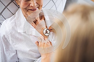 A health visitor examining a sick senior woman lying in bed at home with stethoscope.