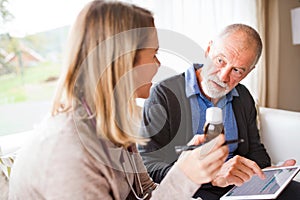 Health visitor and a senior man with tablet during home visit.