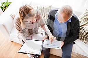 Health visitor and a senior man with tablet during home visit.