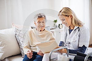 A health visitor and a senior woman sitting on a bed at home, talking.