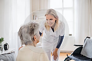 A health visitor talking to a senior woman sitting on bed at home.