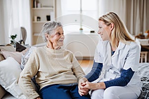 A health visitor talking to a sick senior woman sitting on bed at home.