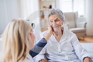 A health visitor talking to a sick senior woman sitting on bed at home.