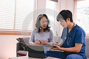 A health visitor is using a tablet to explain to a sick elderly woman how to take her pills.The visitor is taking