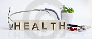 HEALTH the word is written on the wooden cubes and sthetoscope and piils . Medical concept