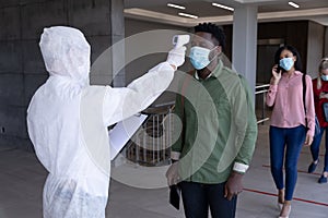 Health worker wearing protective clothes checking temperature of businessman