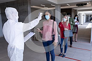 Health worker wearing protective clothes checking temperature of businesswoman