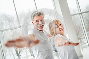 Health and yoga. Senior couple doing yoga pose looking at camera and smiling