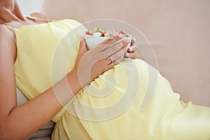 The health of your pregnancy is in your hands. a pregnant woman relaxing on the sofa while eating a fresh salad.