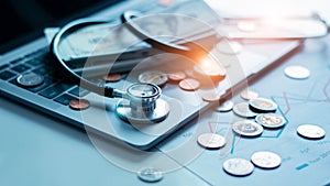 Healthcare business, Doctor stethoscope and coins with stack of cash on laptop. Graph data of business growth on report, Health