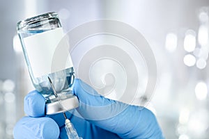 Health care concept with a hand in blue medical gloves holding a vaccine vial with blue liquid and black white label