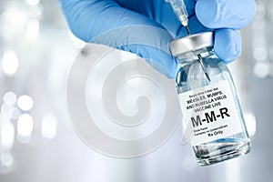 Healthcare concept with a hand in medical gloves holding MMR, measles, mumps, and rubella, vaccine vial photo