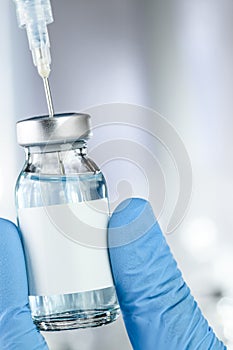 Healthcare concept with a hand in medical gloves holding a vaccine vial with blue liquid and black white label