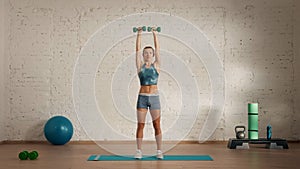 Healthcare creative advertisement concept. Woman fitness coach in the room holding dumbbells over head.