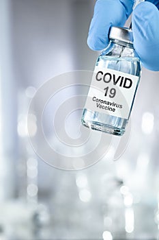 Healthcare cure concept with a hand in blue medical gloves holding Coronavirus, Covid 19 virus, vaccine vial