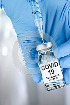 Healthcare cure concept with a hand in blue medical gloves holding Coronavirus, Covid 19 virus, vaccine vial