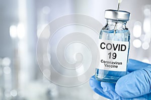 Healthcare cure with a hand in blue medical gloves holding Coronavirus, Covid 19 virus, vaccine vial