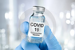 Healthcare cure with a hand in blue medical gloves holding Coronavirus, Covid 19 virus, vaccine vial