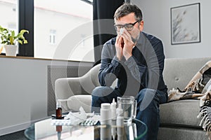 healthcare, flu, hygiene and people concept - sick senior man with paper wipe blowing his nose at home