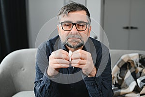 healthcare, flu, hygiene and people concept - sick senior man with paper wipe blowing his nose at home