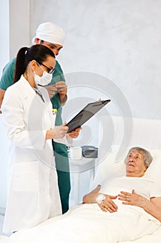 Healthcare in hospital. male surgeon and female doctor or nurse making medical examination of old lady lying in bed and