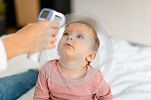 Healthcare for infant child. Mother measuring temperature of her baby girl with infrared thermometer, closeup