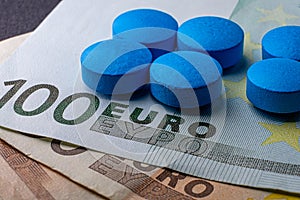 Healthcare insurance. Blue tablets pill macro on 100 euro bill. Drug abuse. Health funds