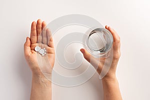 Healthcare and medical concept. Person holding pills in one hand and glass of water in the another hand