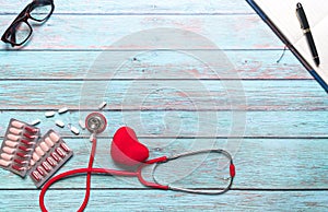 Healthcare and medical concept red stethoscope and medicine on the blue wooden background