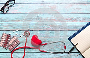 Healthcare and medical concept red stethoscope and medicine on the blue wooden background