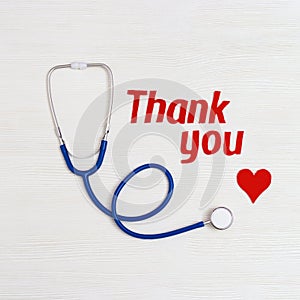 Healthcare and medical concept. Stethoscope blue colored, red heart and text thank you on white wooden background with