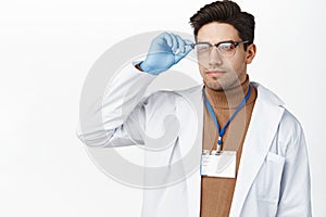 Healthcare and medical concept. Young male doctor in hospital uniform, wearing glasses and name tag, looking aside with