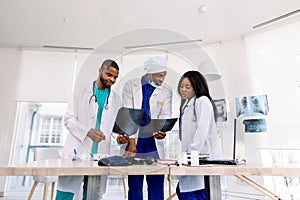 Healthcare, medical: Group of three young African doctors, two men and woman, discuss and looking x-ray in a clinic or