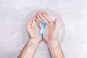 Healthcare and medicine concept - blue ribbon of prostate cancer awareness in male hands, achalasia and adrenocortical cancer, on photo