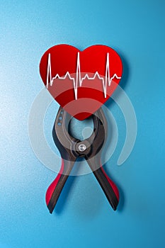 Healthcare and medicine concept - close up of a red heart with an ecg line clamped in a vise for resuscitation. Salvation of life