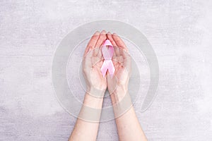 Healthcare and medicine concept - female hands hold pink breast cancer awareness ribbon on gray background