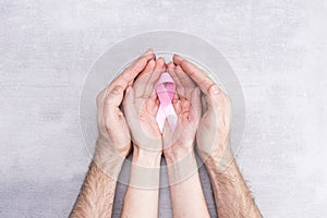 Healthcare and medicine concept - female and male hands hold pink breast cancer awareness ribbon on gray background