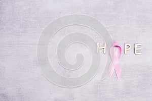 Healthcare and medicine concept - pink breast cancer awareness ribbon and letters of the word HOPE on a gray background with place