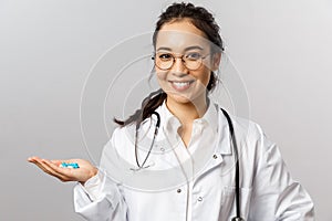 Healthcare, medicine and pharmacy concept. Portrait of young asian female doctor holding pills, taking care of patient