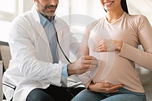 Healthcare, prenatal care. Male doctor examining pregnant woman& x27;s belly using stethoscope, listening baby& x27;s