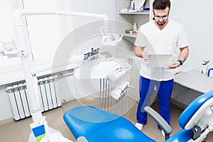 Healthcare, profession, stomatology and medicine concept - smiling male young dentist over medical office background