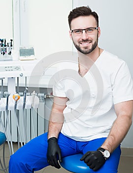 Healthcare, profession, stomatology and medicine concept - smiling male young dentist over medical office background