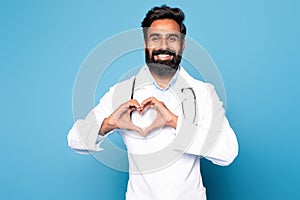 Healthcare professional. Happy indian male doctor showing heart gesture with hands posing on blue background