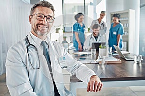 Healthcare, smile and portrait of senior doctor at desk in teaching hospital office with nurses and medical students