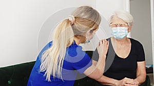 Healthcare support. Young caring caucasian blond-haired female nurse in dark blue uniform supporting her elderly lady