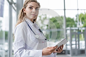 Healthcare, technology and medicine concept - smiling female doctor with stethoscope taking notes at tablet pc computer.